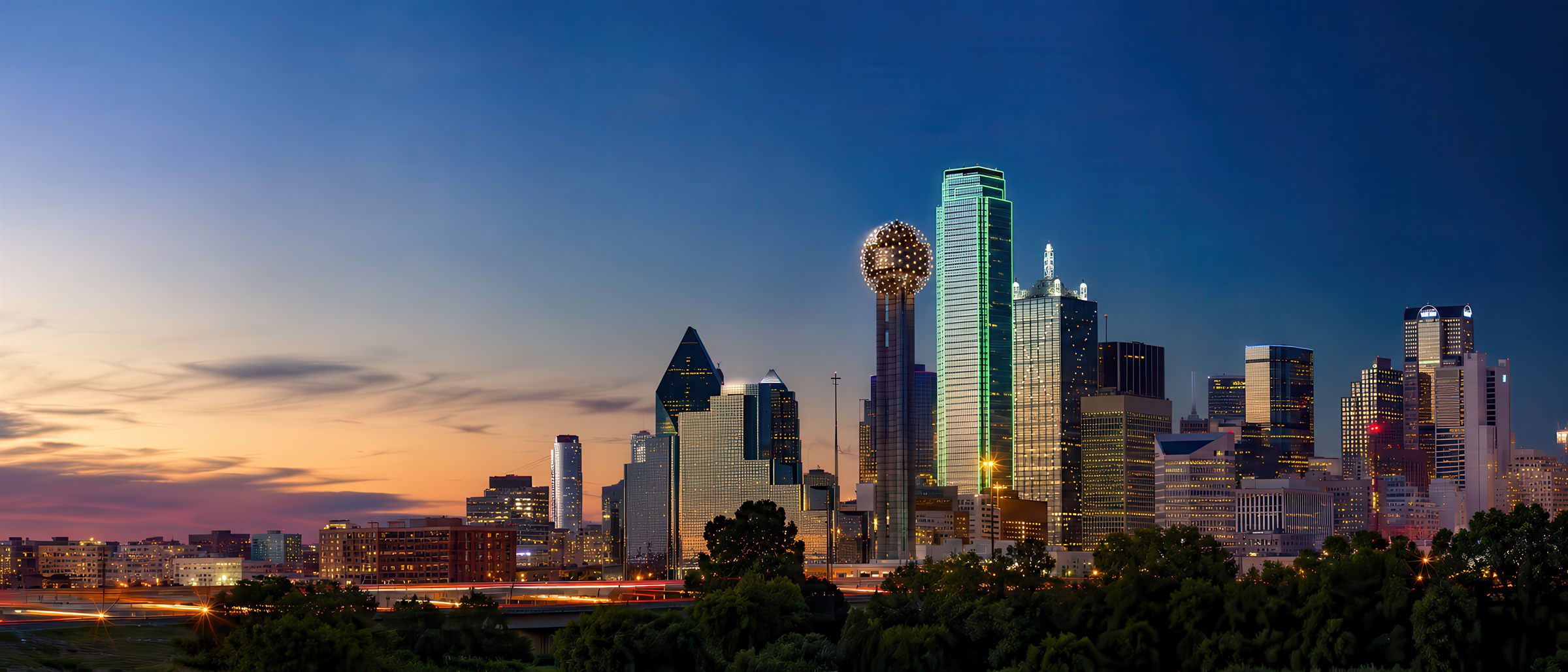 The Dallas skyline glowing at blue hour, a warm horizon fading over the city